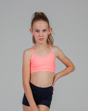 Young girl wearing a pink sports bra and black shorts on a gray background