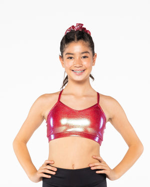 A young gymnast wearing a red Mystique crop top with a shiny, metallic fabric. She has her hands on her hips and is smiling at the camera.