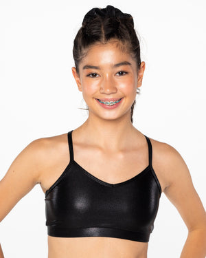 A young gymnast wearing a red Mystique crop top with a shiny, metallic fabric. She has her hands on her hips and is smiling at the camera.