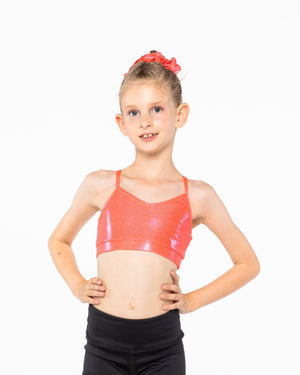 A young gymnast wearing a red Mystique crop top with a shiny, metallic fabric. She has her hands on her hips and is smiling at the camera.