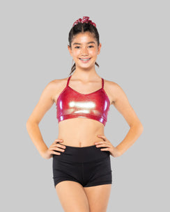 A child wearing a red and black sleeveless dance top and black shorts, standing with one hand on her hip.