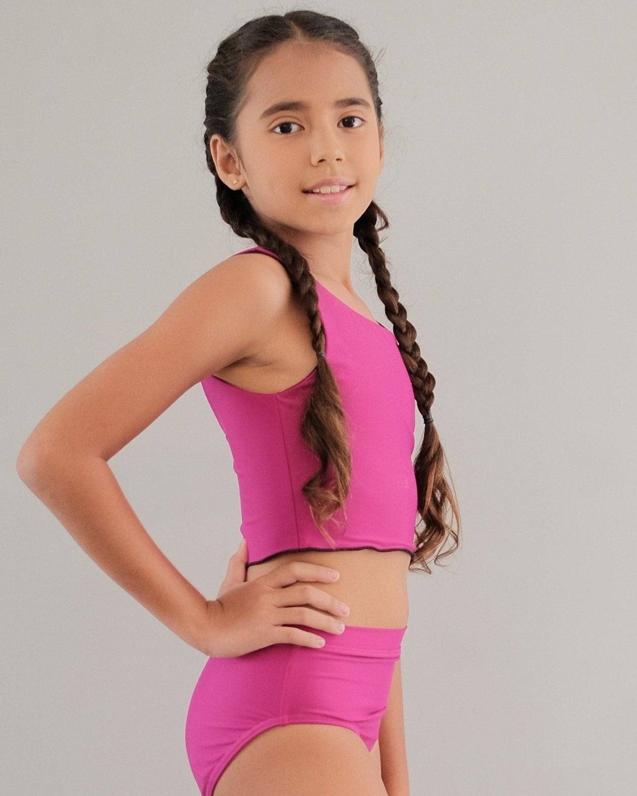 A child wearing pink and black dance and swim briefs, standing with one hand on her hip.
